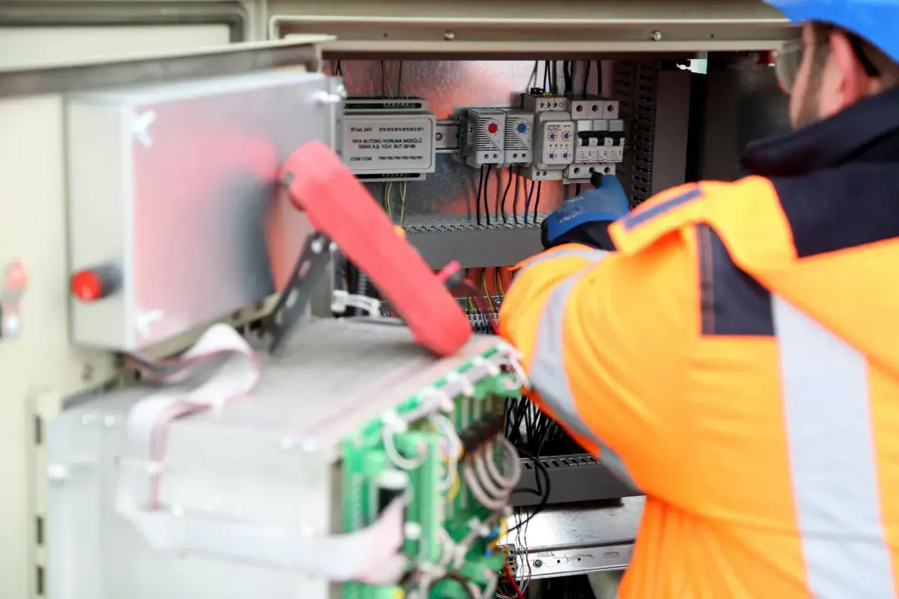 Elektryk w pomarańczowej kamizelce pracuje przy panelu sterowania, podłączając kabel neutralny.