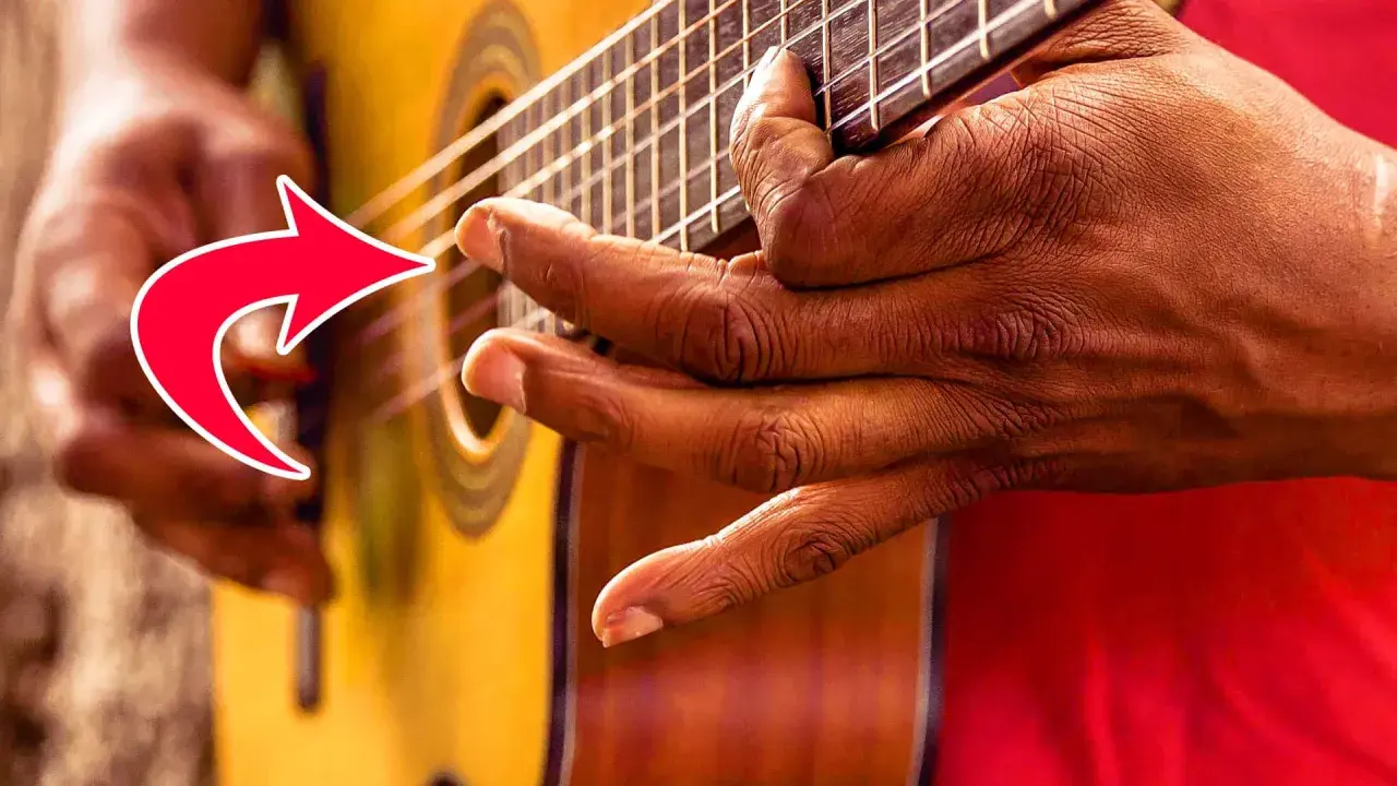 Hände spielen Fingerstyle Gitarre. Ein roter Pfeil zeigt auf die Finger, die die Saiten greifen.