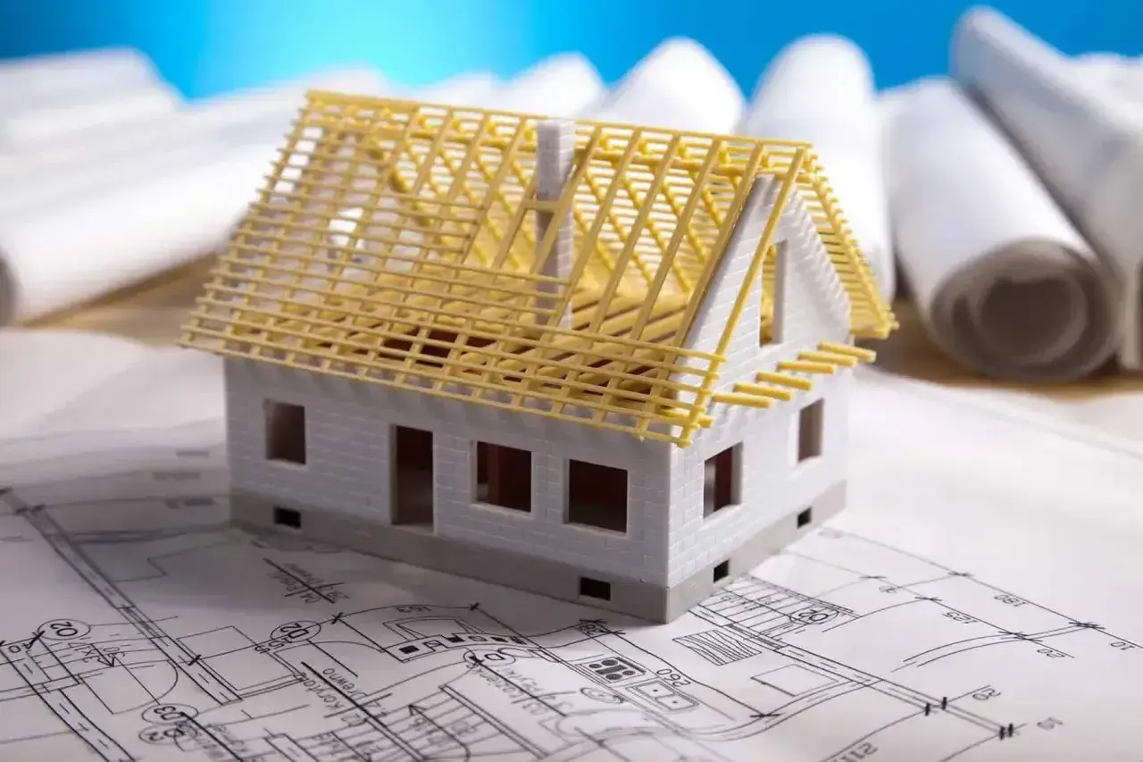 Model domu na planach architektonicznych, z widoczną konstrukcją dachu. Zastanawiasz się, ile kosztuje adaptacja projektu?