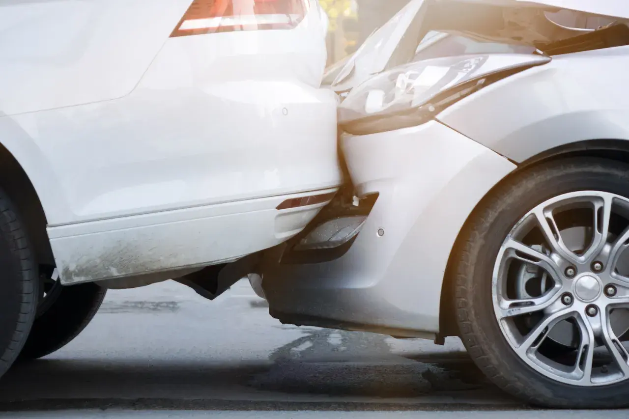 Zwei Autos sind kollidiert, ein weißes und ein silbernes. Der Unfall beim Ausparken hat die Stoßstangen und Scheinwerfer beschädigt.