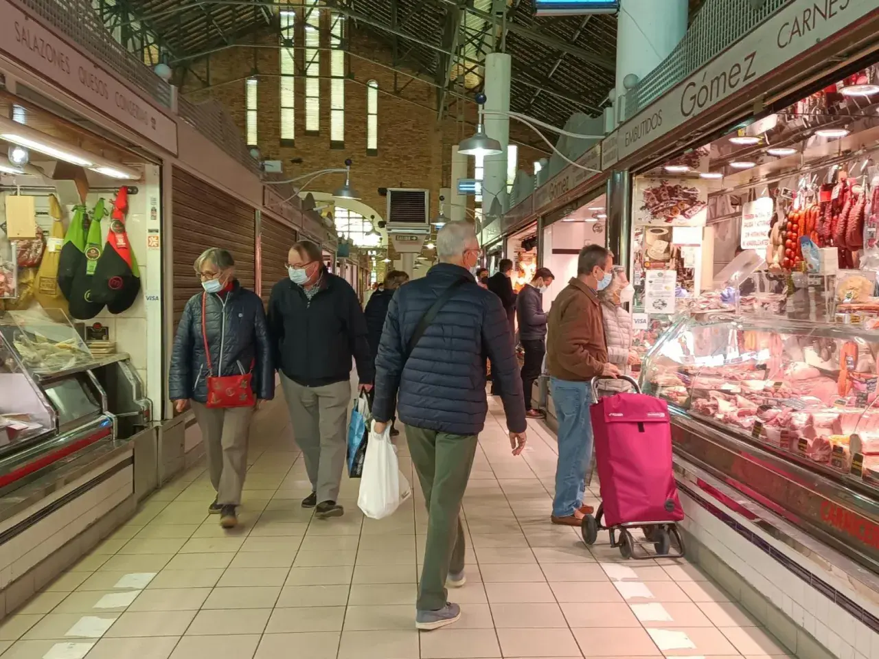 Gente comprando en el mercat central d'Alacant, con puestos de embutidos y carnes.