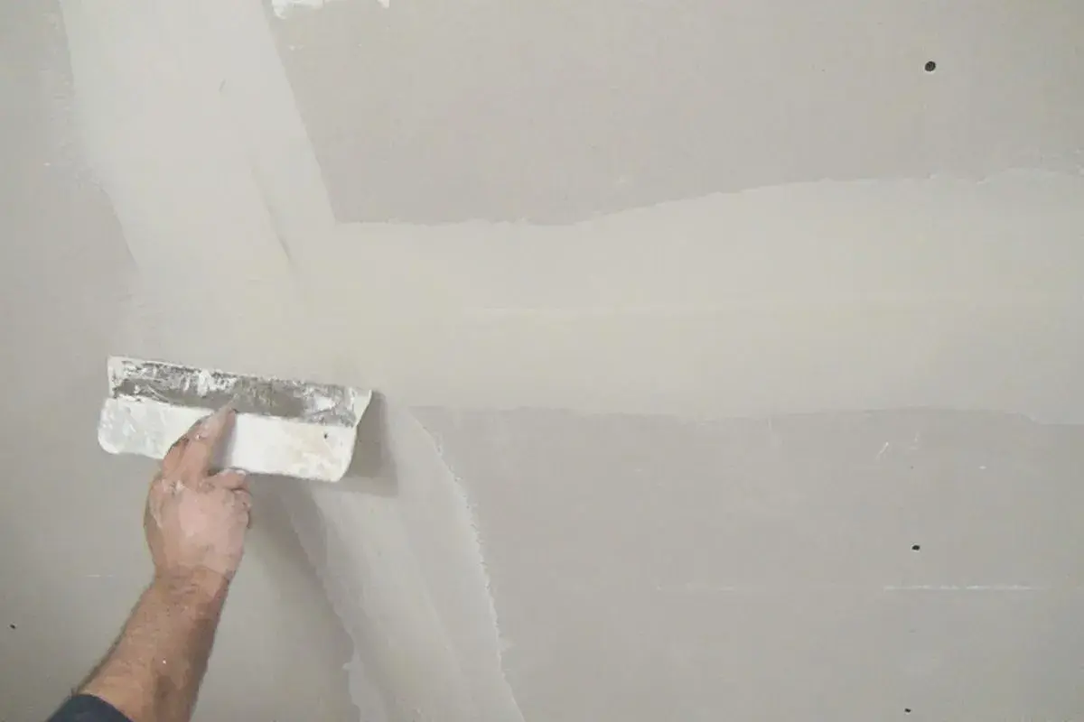 Hand verspachtelt Rigipsplatten mit einem Spachtel. Die Naht wird geglättet, um eine ebene Oberfläche für die weitere Bearbeitung zu schaffen.