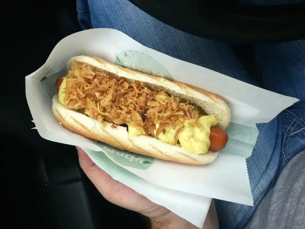 Pyszny hot dog z chrupiącą cebulką i sosem, idealny na szybki posiłek. Gdzie kupić sosy z Orlenu? Warto sprawdzić na stacji!