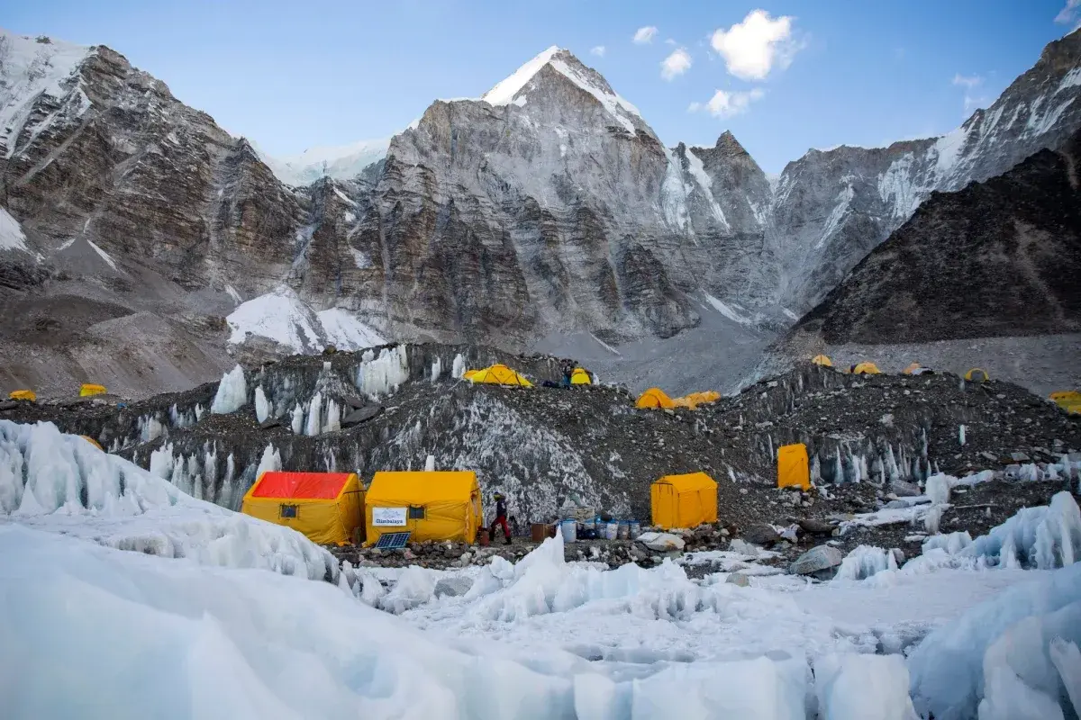 Obóz u podnóża Mount Everest, gdzie **mount everest wysokość** jest wyzwaniem. Żółte namioty na lodowcu, w tle majestatyczne, skaliste szczyty.