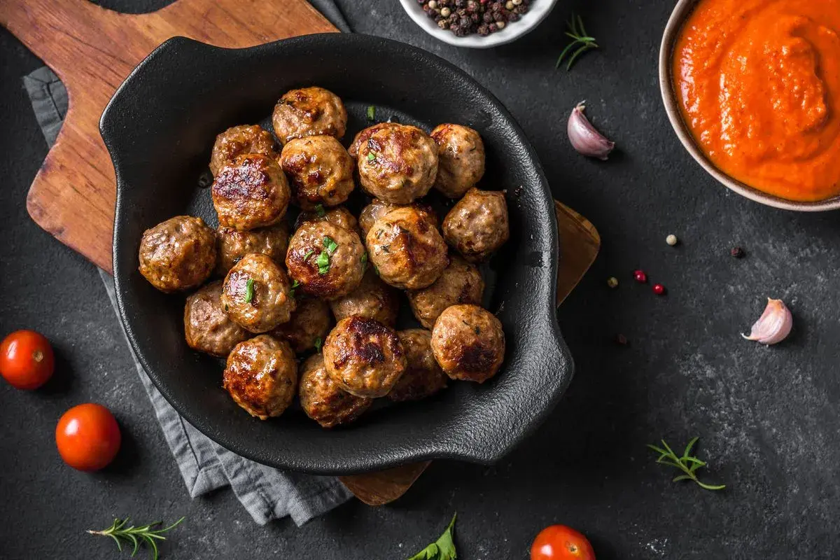 Polpette dorate e succulente, cotte alla perfezione nella friggitrice ad aria, pronte per essere gustate con salsa e pomodorini freschi.