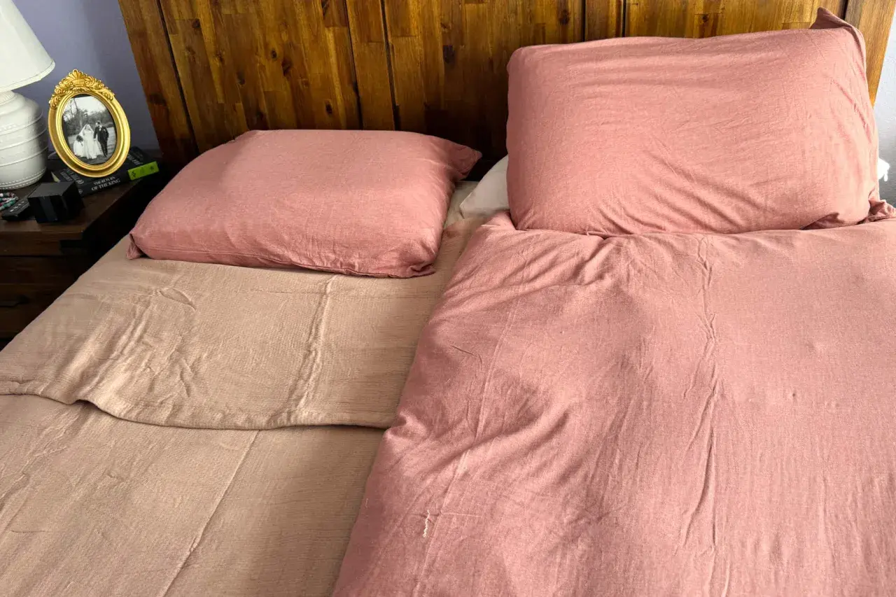 A bedspread can be used as a blanket, as shown by this cozy, pink-covered bed with a wooden headboard.