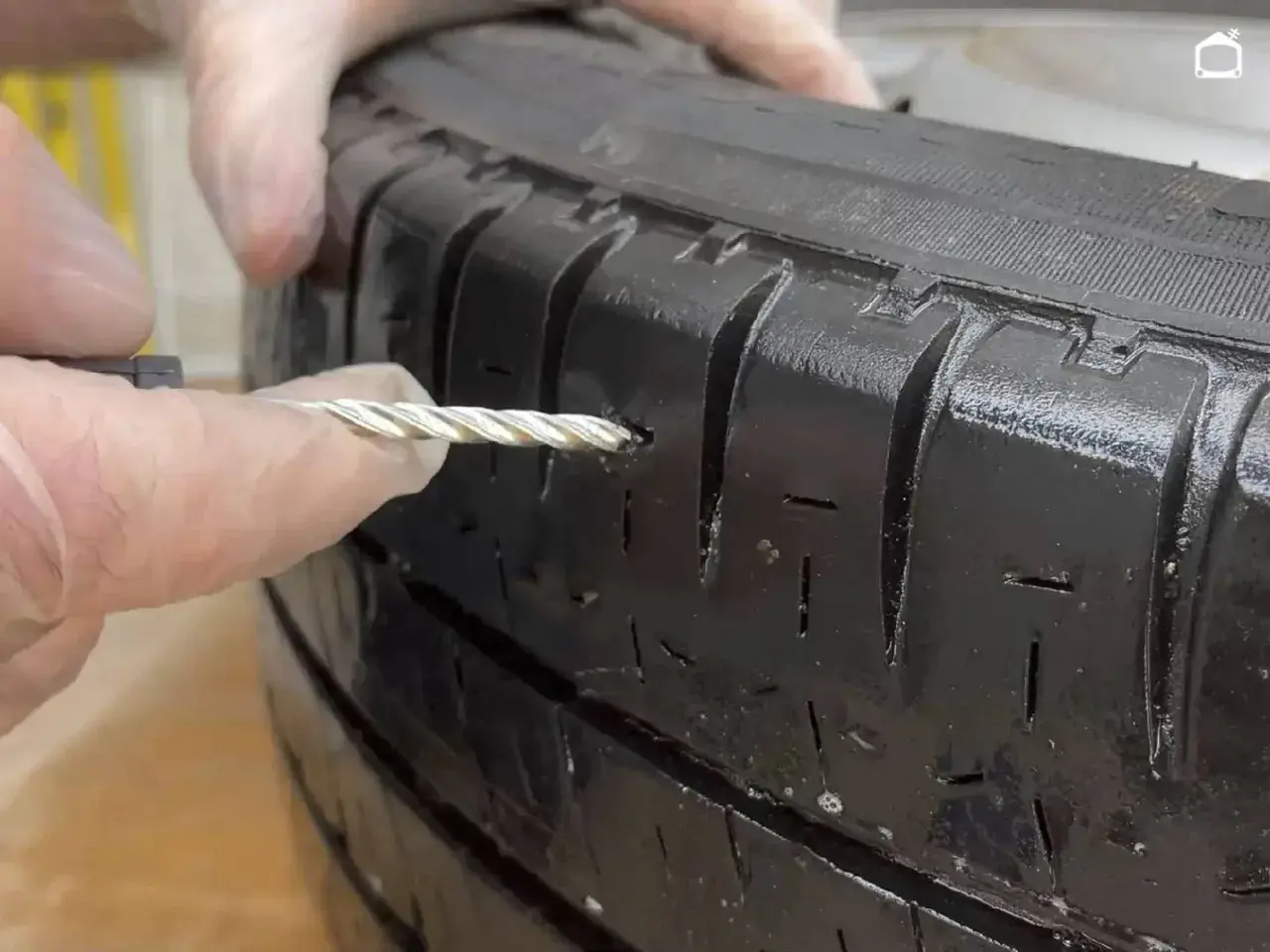Manos con guantes reparando un pinchazo en un neumático con una herramienta.