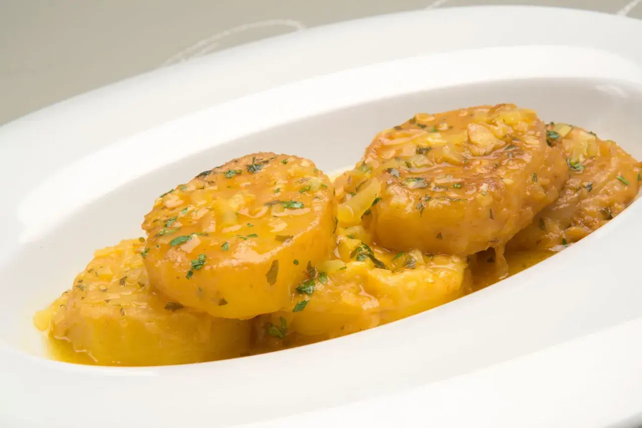 Patatas a la importancia, doradas y jugosas, bañadas en una salsa con ajo y perejil, servidas en un plato blanco.