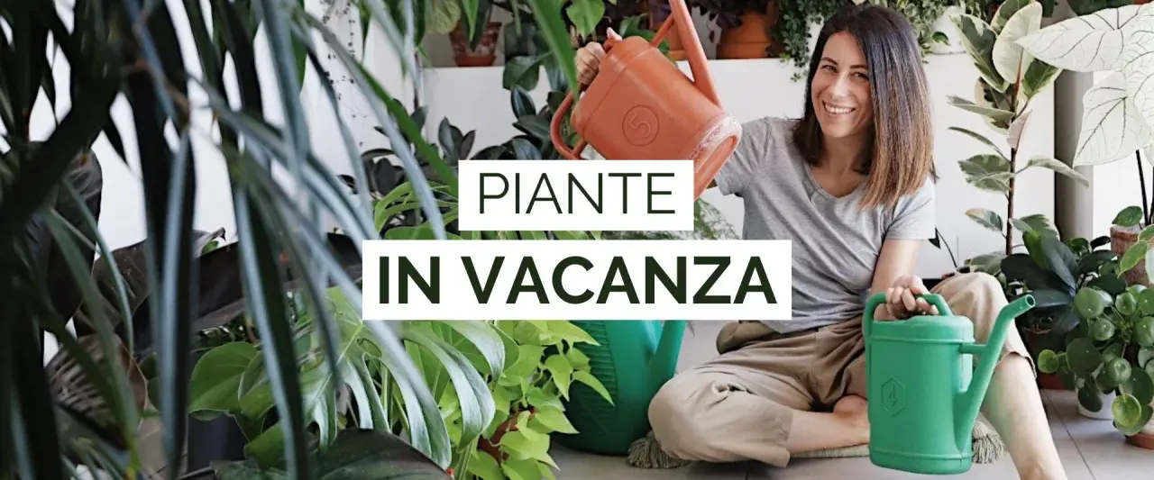 Donna sorridente con annaffiatoi, circondata da piante rigogliose. Impara come innaffiare le piante in vacanza per mantenerle sane.