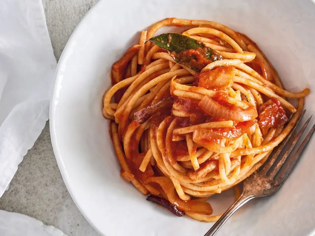 En skål med bucatini all'amatriciana, en klassisk italiensk pastarätt med tomatsås, lök och en lagerblad.