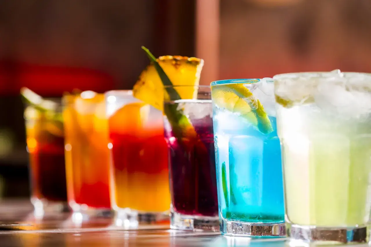 Kolorowe drinki na barze, w tym niebieski koktajl z plasterkiem cytryny, przypominają letnie orzeźwienie, jak Bacardi Razz drink.