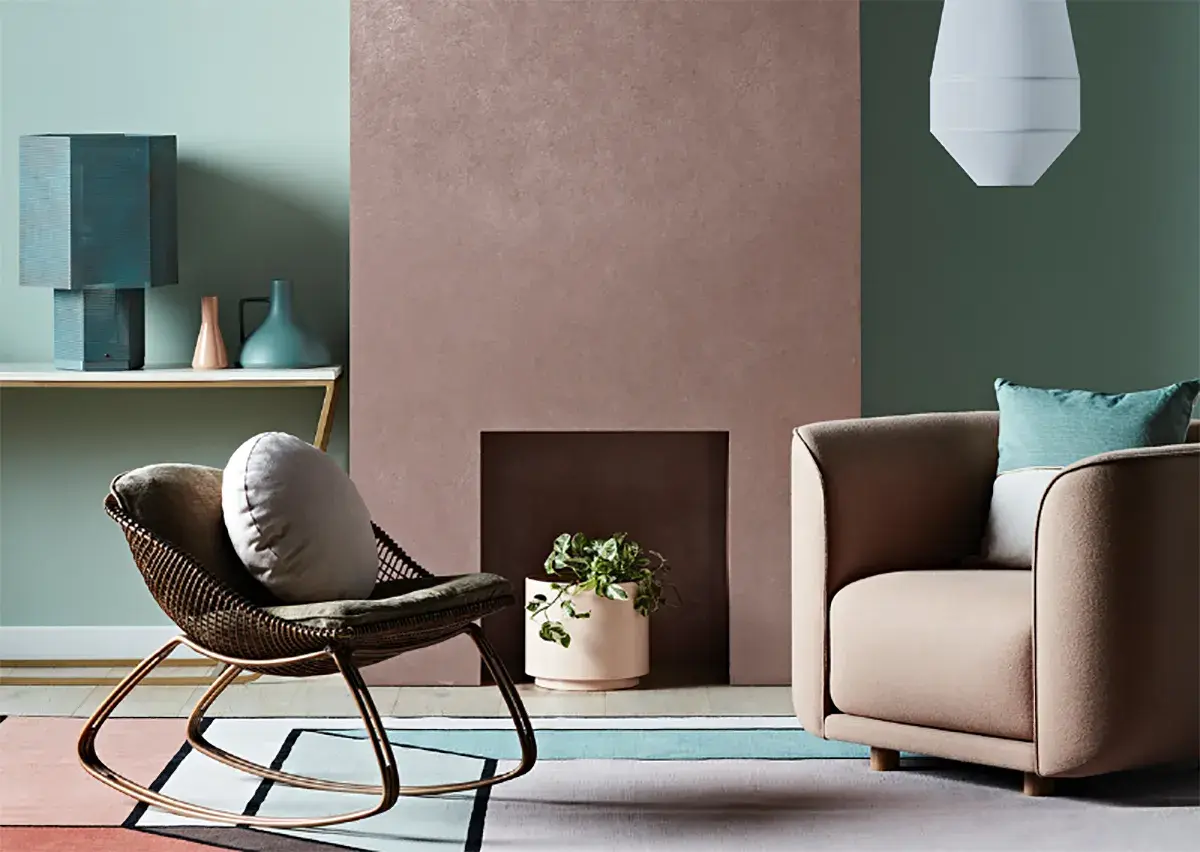 Simulazione abbinamento colori pareti: un salotto con poltrona in vimini, camino rosa e divano beige, su un tappeto geometrico.