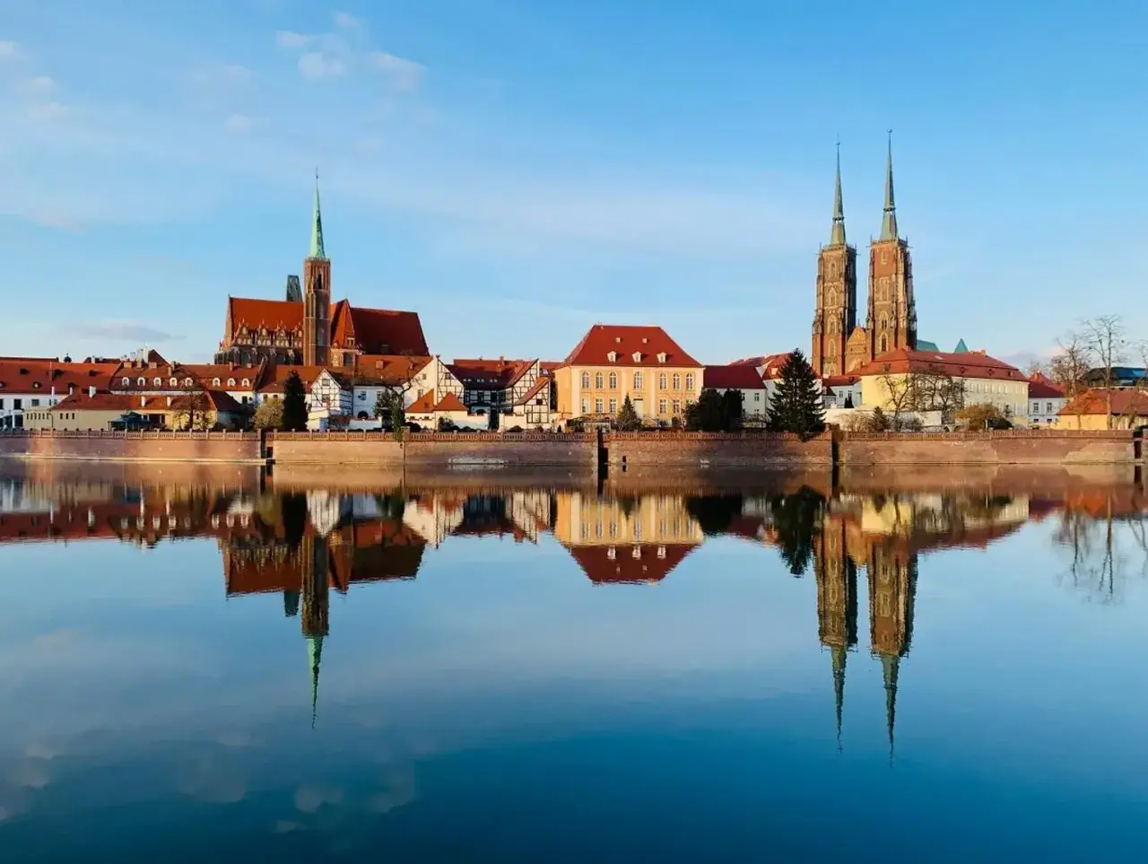 Wrocław wydarzenia na weekend: Katedra i zabytkowe kamieniczki odbijają się w spokojnej tafli Odry.
