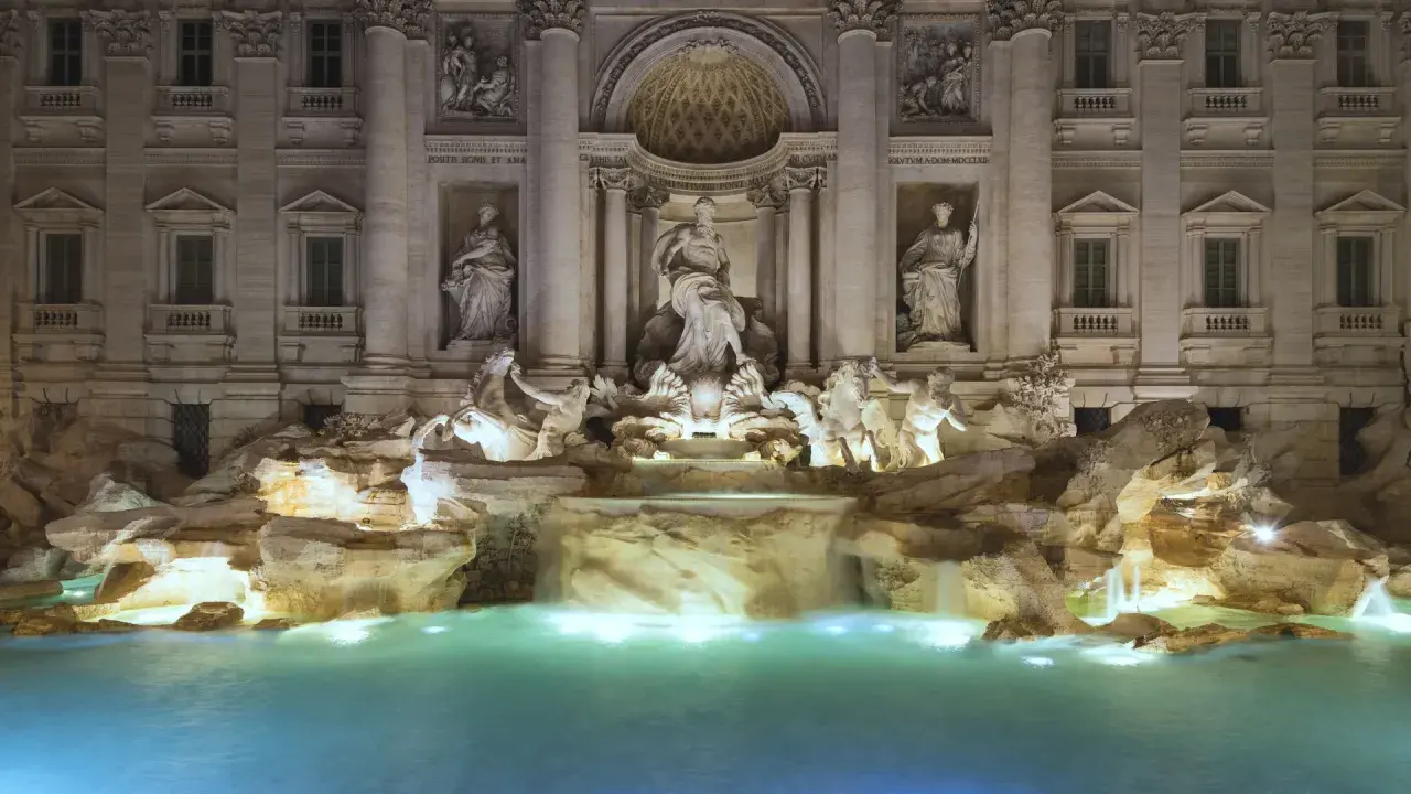 Fontana di Trevi stile barocco, con statue di divinità marine e cavalli marini che emergono da rocce e cascate, illuminata di notte.