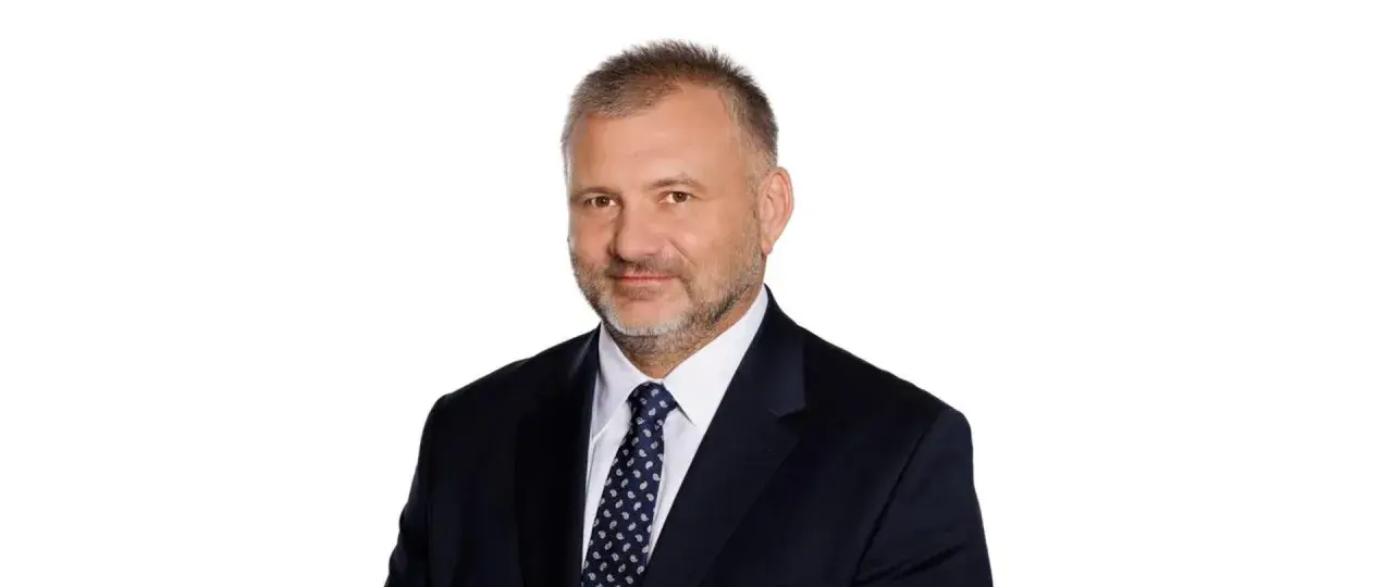Mężczyzna w garniturze i krawacie, z krótkimi włosami i zarostem. Wygląda jak prokurator generalny.