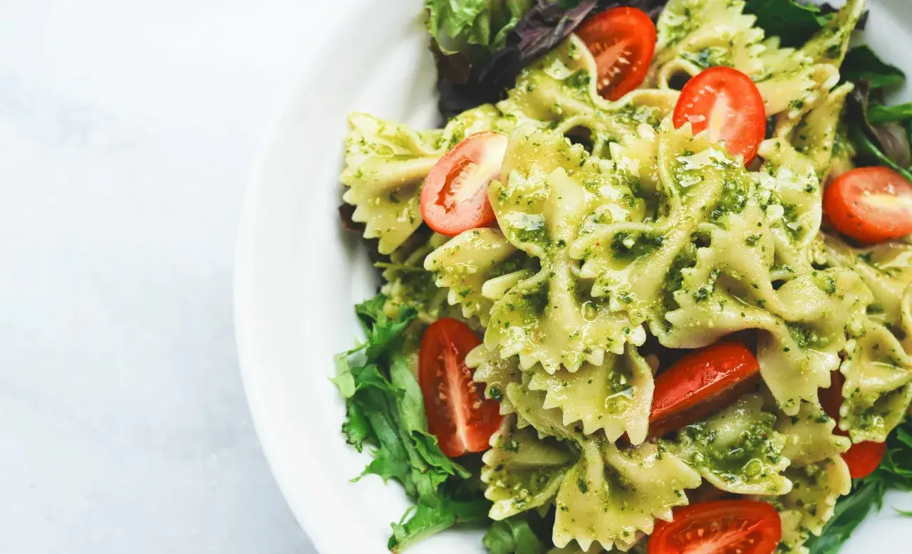Ein köstlicher italienischer Nudelsalat mit Farfalle, Pesto und Kirschtomaten, garniert mit frischem Salat.