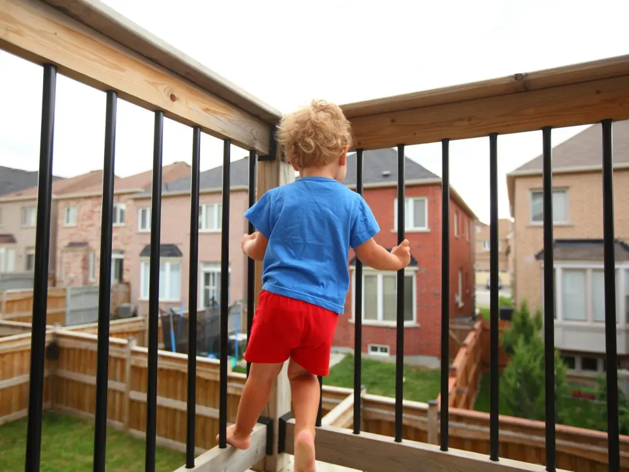 Kleines Kind auf einem sicheren Balkon, das neugierig die Nachbarschaft erkundet.