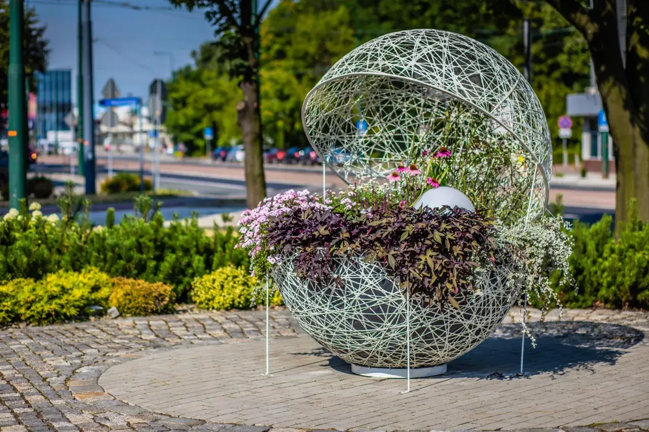 Ozdobna kula z kwiatami, przykład instalacji artystycznej. Wplecione w ażurową konstrukcję rośliny tworzą efektowną kompozycję.