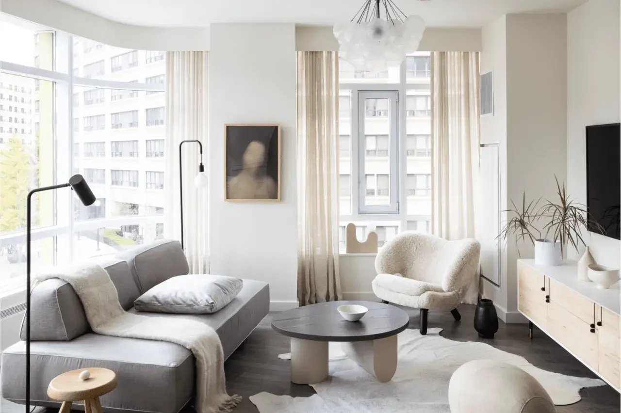 A cozy living room, perfect for learning how to furnish a small apartment. A grey sofa, fluffy armchair, and round coffee table create a welcoming space.