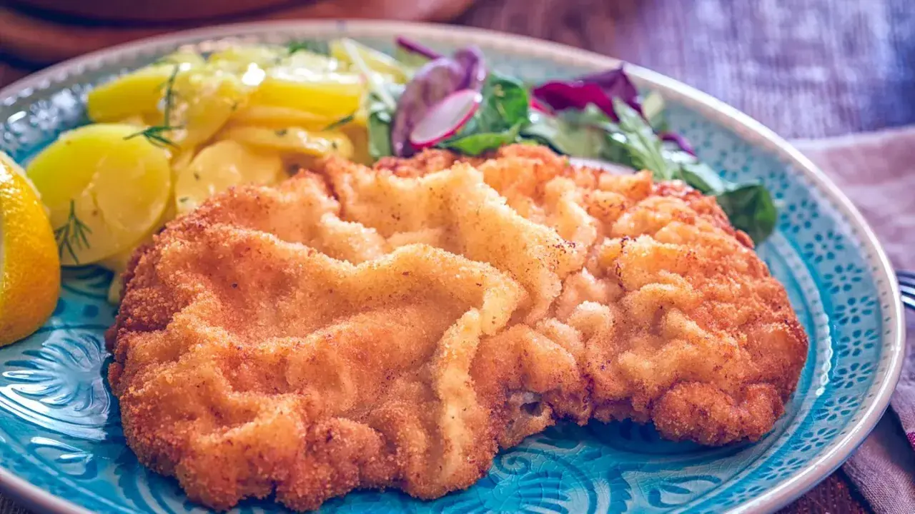 Ein knuspriges Wiener Schnitzel mit Kartoffelsalat und Zitrone auf einem blauen Teller.