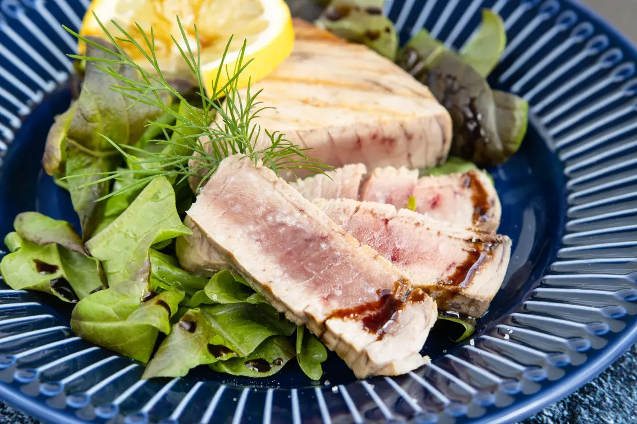 Saftiges Thunfisch Steak, medium gebraten, serviert mit frischem Salat, Dill und einer Zitronenspalte auf einem blauen Teller.
