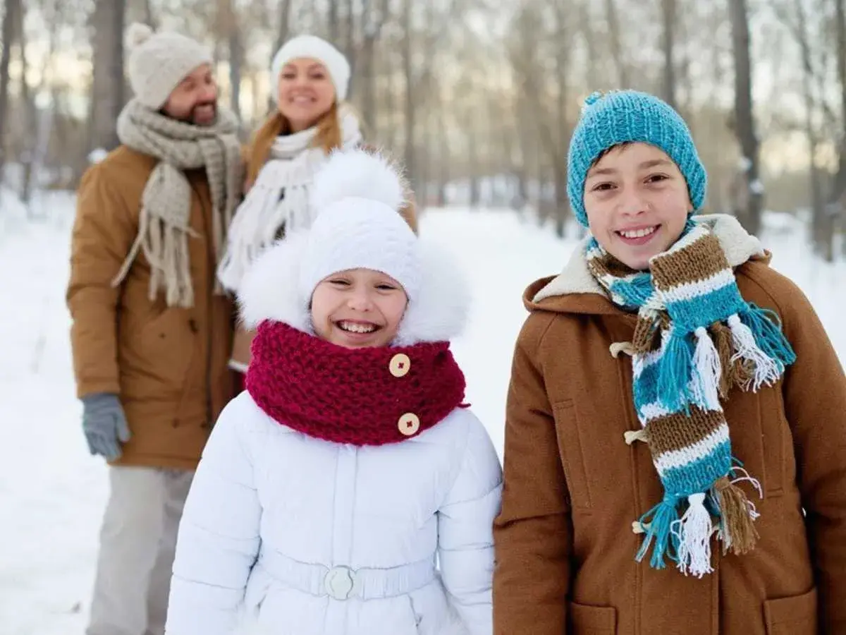 Familia sonriendo en un día de **invierno para niños**. Los niños al frente llevan abrigos y bufandas coloridas.