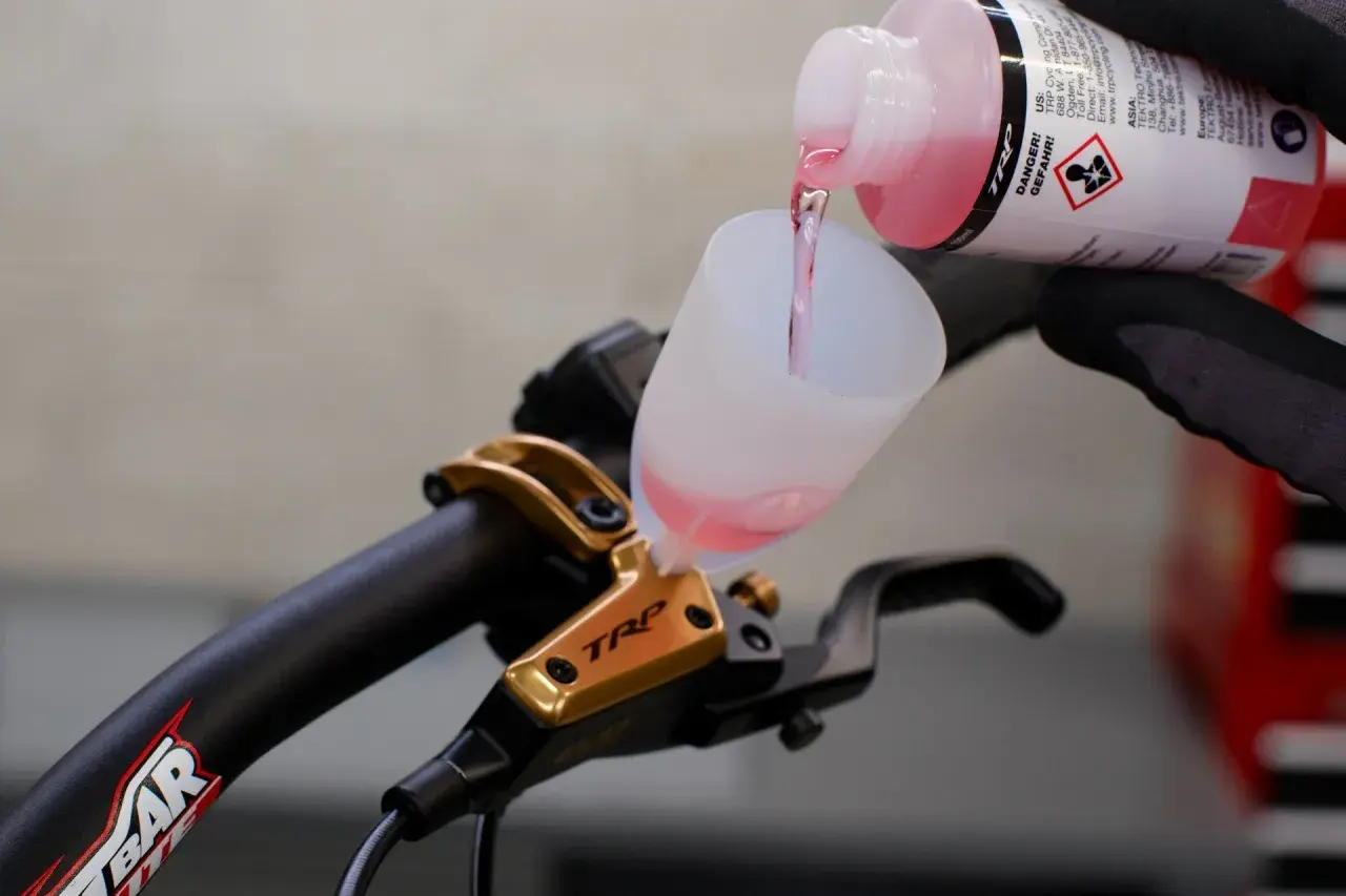 Adding brake fluid without bleeding is not recommended. This image shows pink fluid being poured into a funnel on a TRP brake lever.