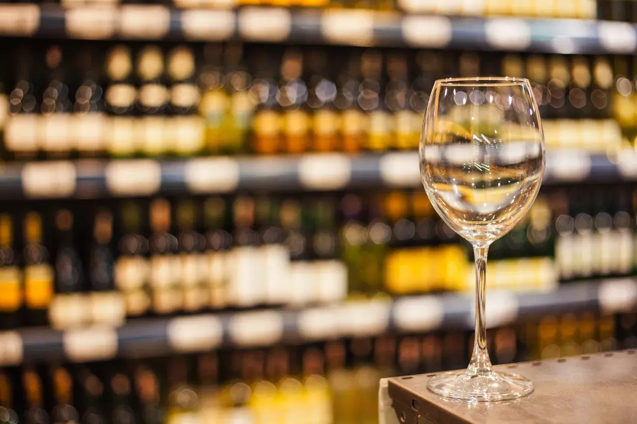 Verre à vin vide sur un comptoir, devant des étagères remplies de bouteilles. L'ambiance évoque une dégustation de vin à Paris.