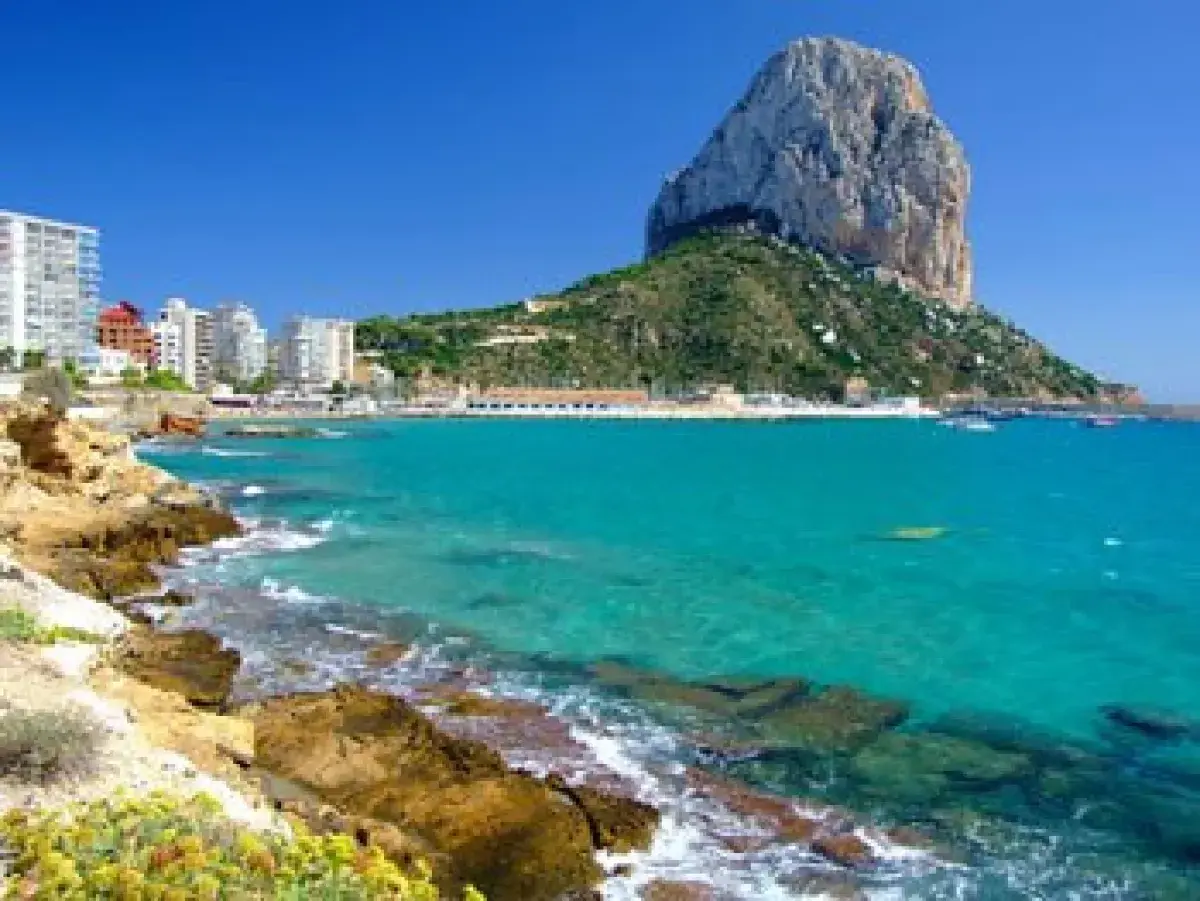 Vista del natural park of Penyal d'Ifac con aguas turquesas, rocas y edificios costeros.