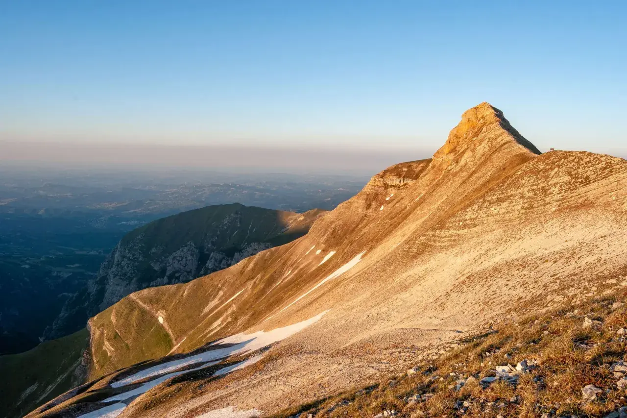 Alba dorata sulla Sibilla Appenninica, con valli nebbiose e un rifugio solitario in vetta.