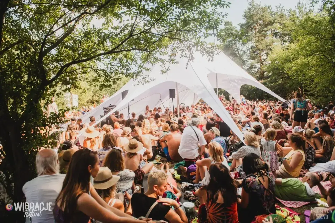 Tłum ludzi siedzi pod białym namiotem na jednym z letnich festiwali w Polsce.