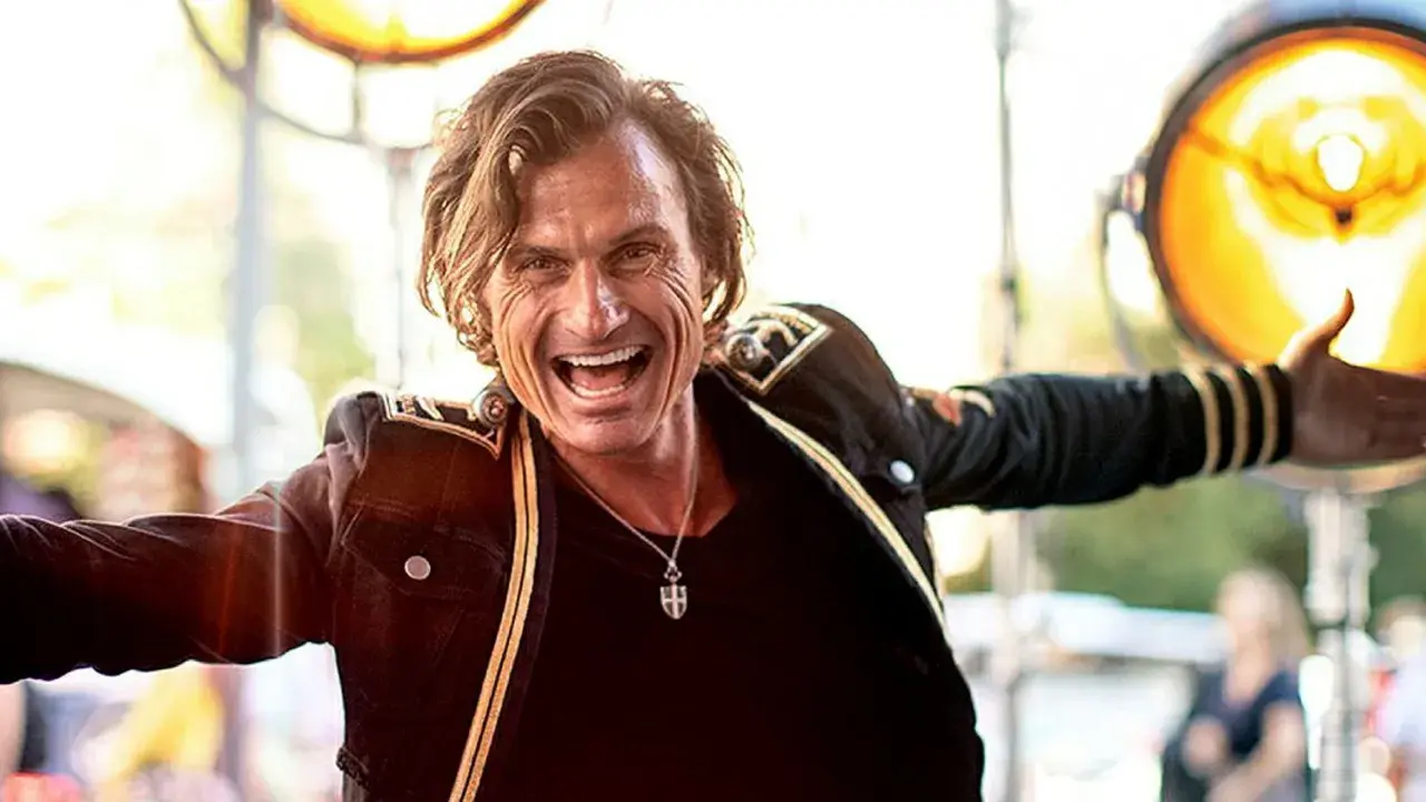 Petter Stordalen, trots sin ålder, strålar av energi i en mörk jacka med gulddetaljer. Han ler brett och gestikulerar.