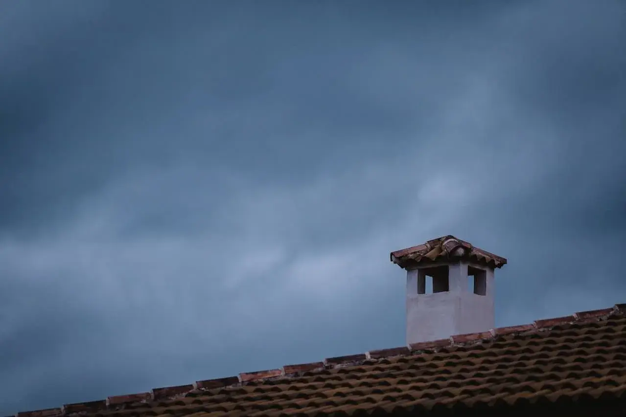 Komin na dachu, jakby pokryty folią w płynie, na tle burzowego nieba.
