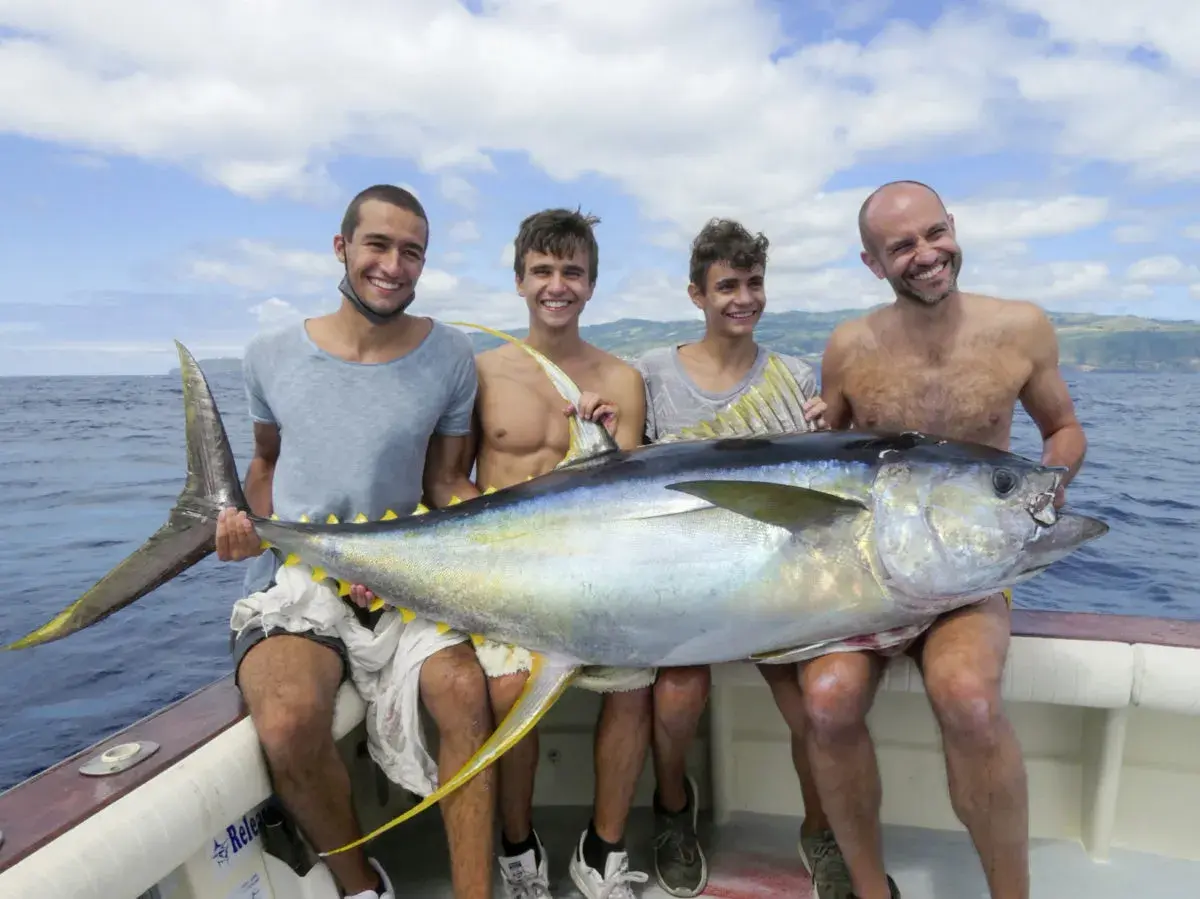 Vier Männer präsentieren stolz einen riesigen Thunfisch auf einem Boot vor den Azoren. Ein erfolgreicher Tag beim **Azoren Angeln**!