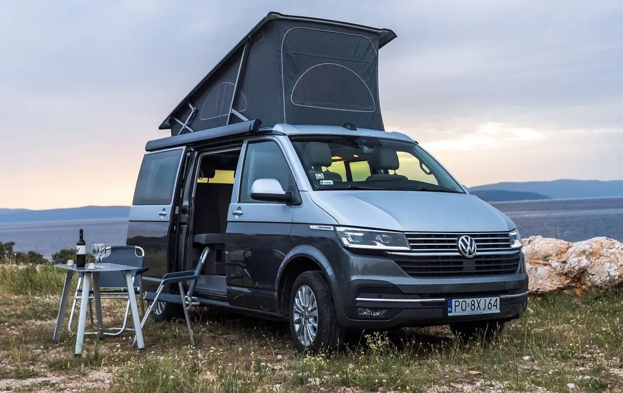 Szary kamper VW California z podniesionym dachem, idealny na wakacje. Poznaj jego wymiary i możliwości podróżnicze.