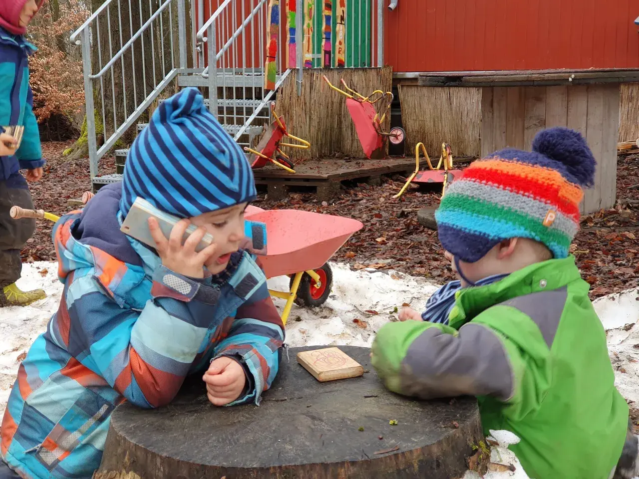 Zwei Kinder im Wald Kindergarten spielen mit einem Spielzeugtelefon und einem Holzklotz.