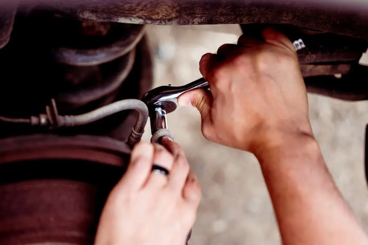 Ręce z kluczem nasadowym próbują odkręcić wyrobioną śrubę imbusową, która jest częścią mechanizmu samochodowego.