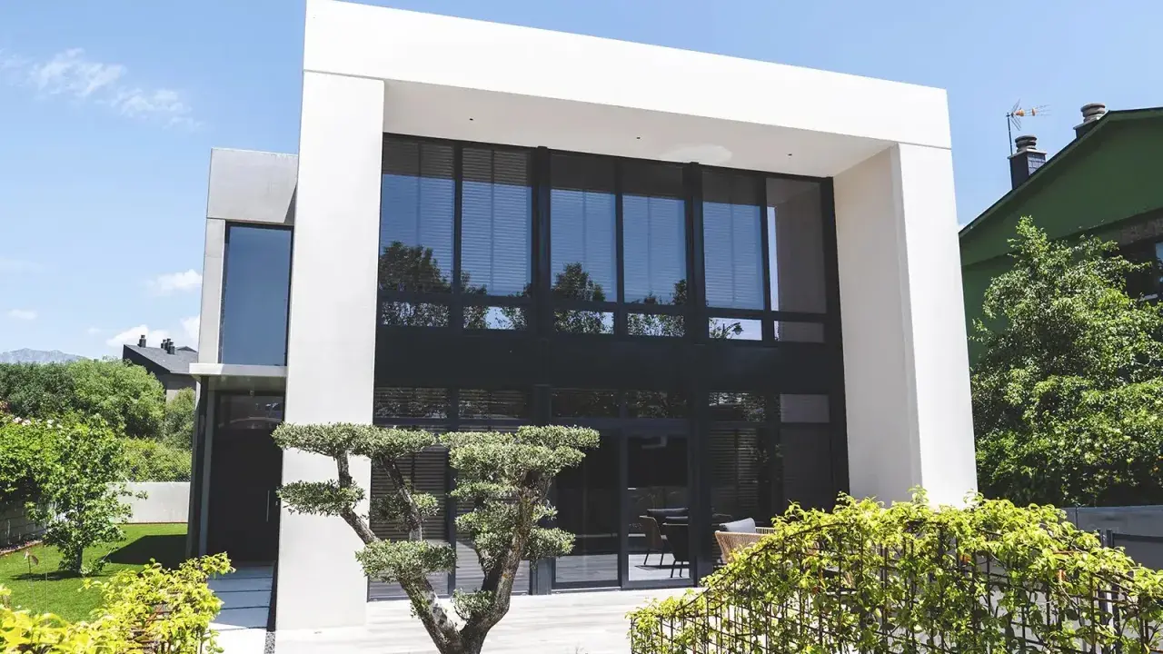 Moderna casa con fachada gris y beige, grandes ventanales y jardín cuidado.