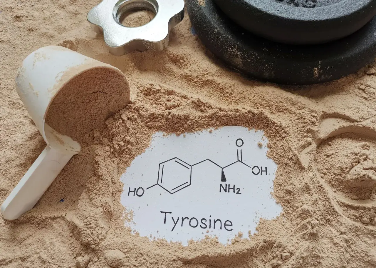 Proszek proteinowy, miarka i ciężarki. Na białej kartce wzór chemiczny i napis "Tyrosine". Tyrozyna co to? Aminokwas wspierający trening.