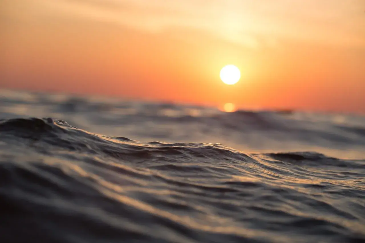 Olas suaves reflejan el atardecer anaranjado. Es como soñar con agua de mar, una paz que te envuelve.