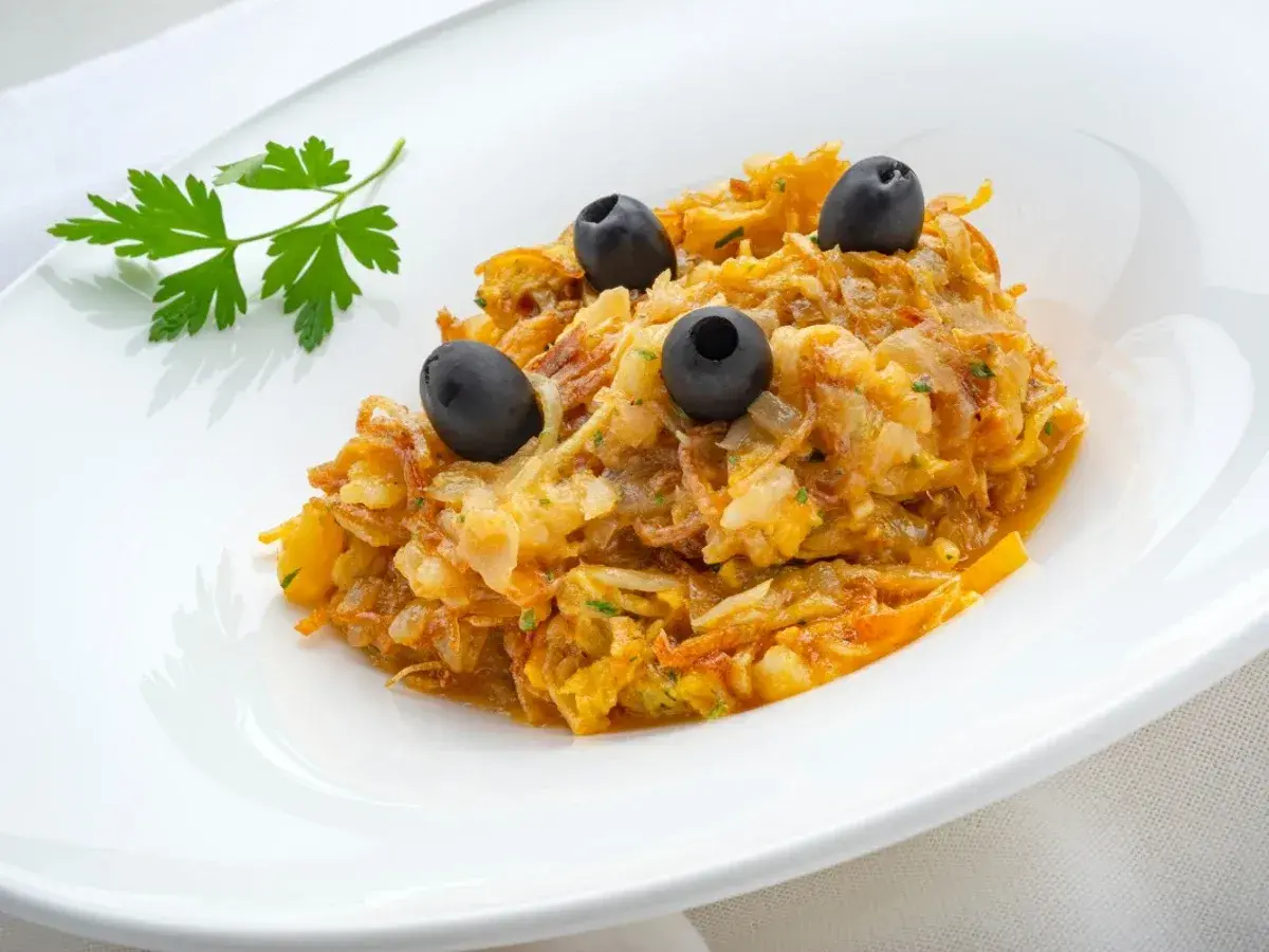 Delicioso revuelto de bacalao con aceitunas negras y perejil fresco, servido en un plato blanco.