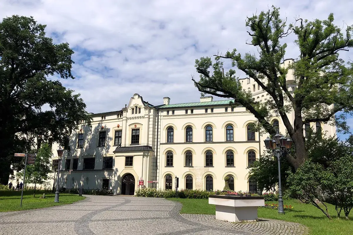 Zamek w Żywcu, okazała budowla z białymi ścianami i licznymi oknami, otoczony zielenią i starymi drzewami.