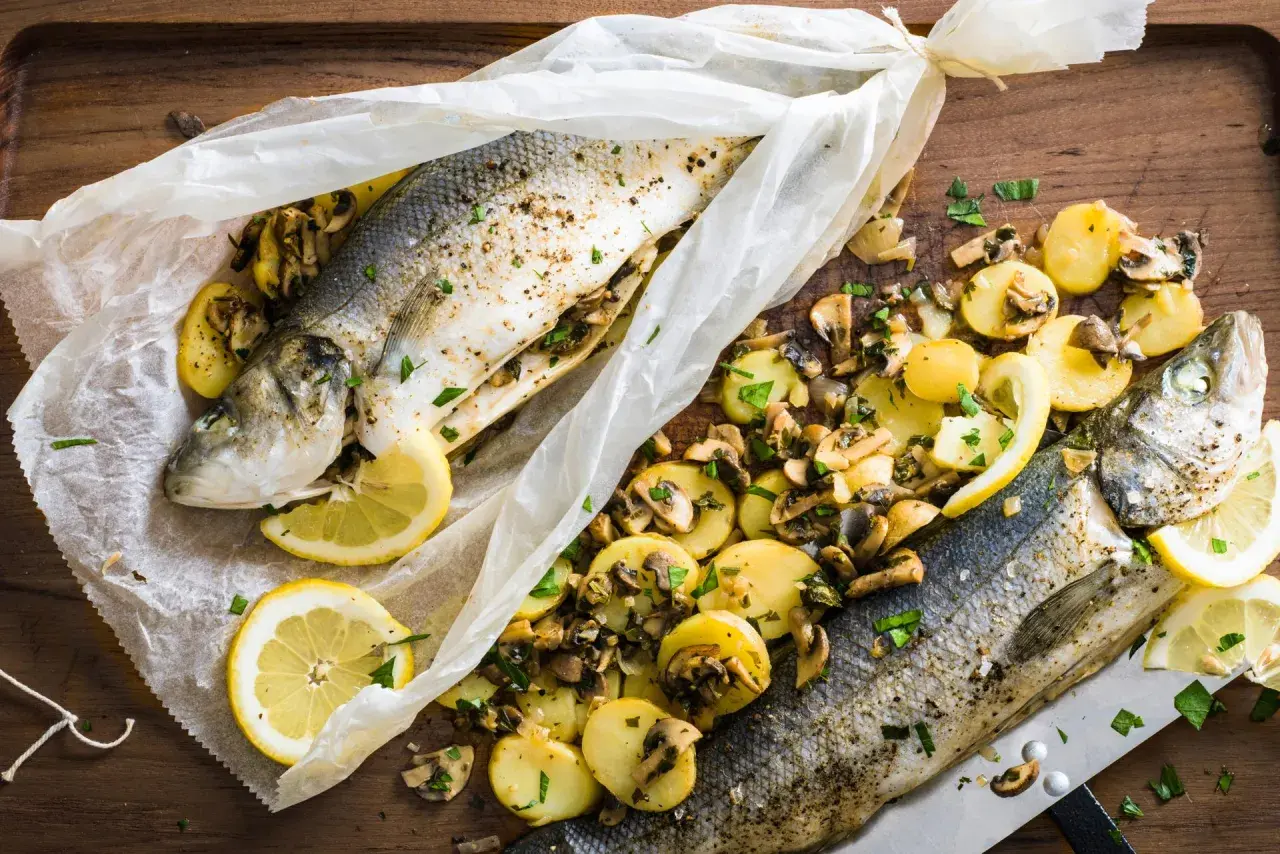 Deux bars en papillote au barbecue, accompagnés de pommes de terre et champignons, citron et persil.