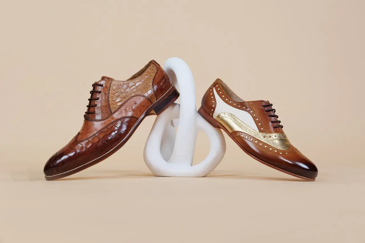Comment porter des richelieu femme : deux paires de chaussures élégantes en cuir marron, ornées de textures et de détails dorés, posées sur un socle blanc.