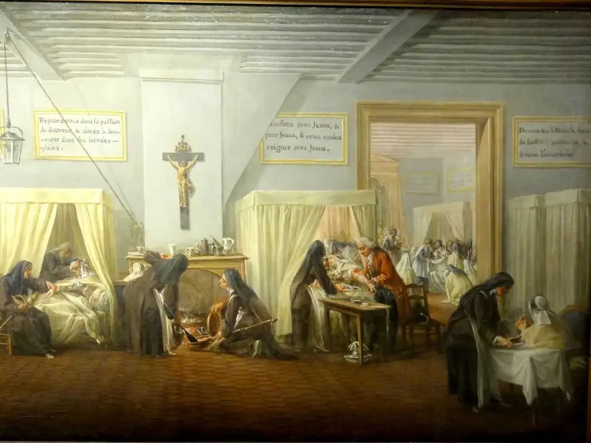 L'hôpital qui se fout de la charité : des religieuses soignent des malades, mais l'une d'elles semble négliger un patient. Une scène ironique.