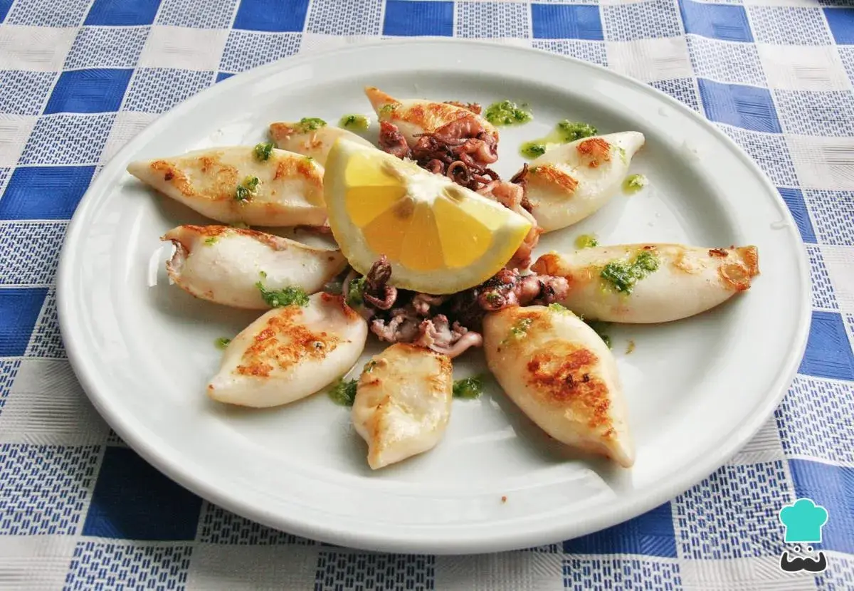 Chipirones a la plancha, tiernos y dorados, servidos con limón y un toque de perejil picado. Un plato sencillo y delicioso.