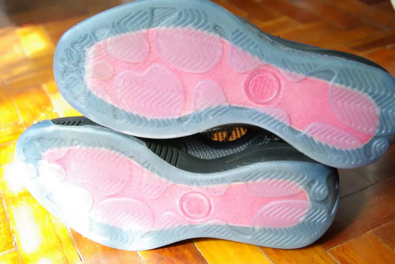 Soles of two black sneakers with pink grip zones and clear rubber outsoles. These shoes are designed to maximize traction, offering a great solution for how to make shoes more grippy.