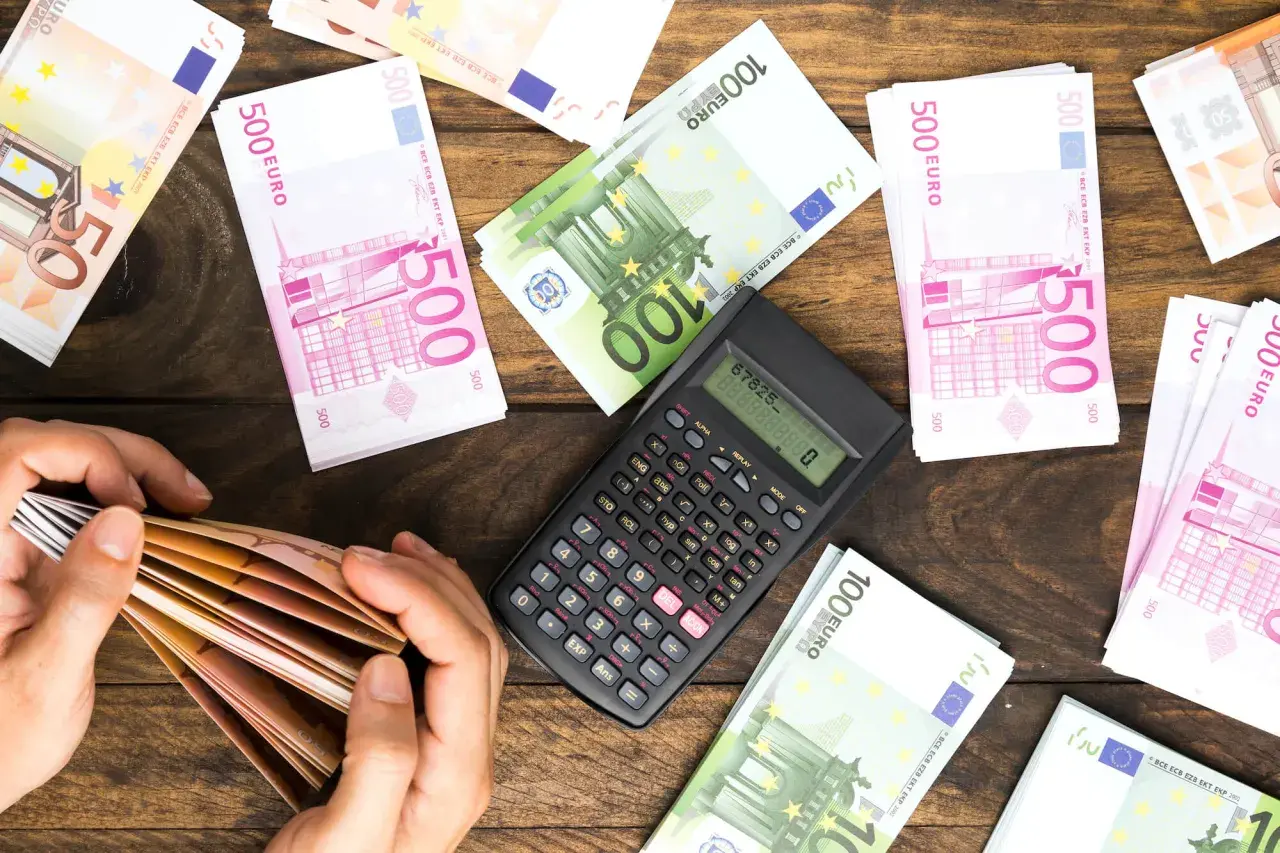 Ręce liczą banknoty euro. Obok kalkulator i stosy pieniędzy. Planowanie spadku dla obcej osoby i podatek od niego.