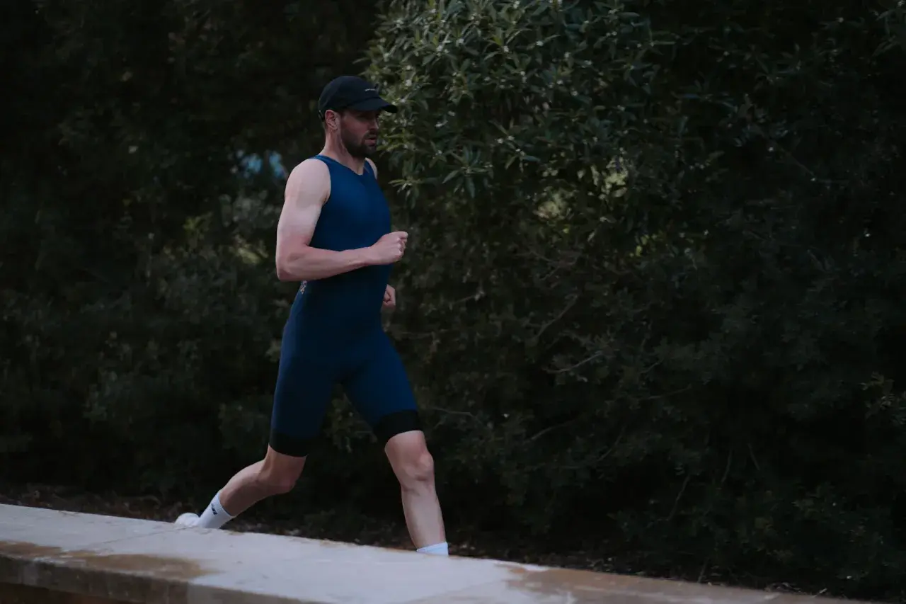 Mann in dunkelblauem Triathlonanzug läuft vor dunklem Grün.