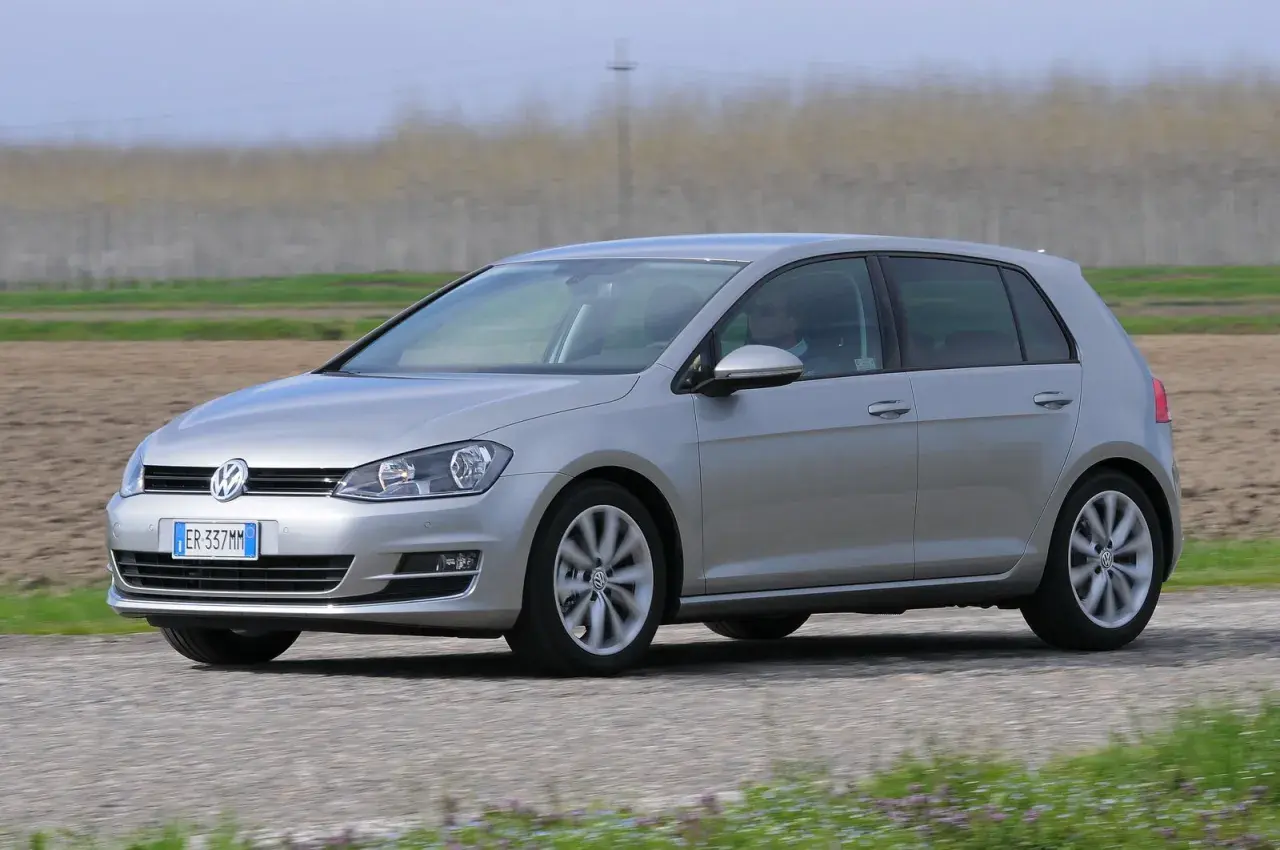 Volkswagen Golf 1.6 TDI argento in movimento su strada sterrata, con campi coltivati sullo sfondo.